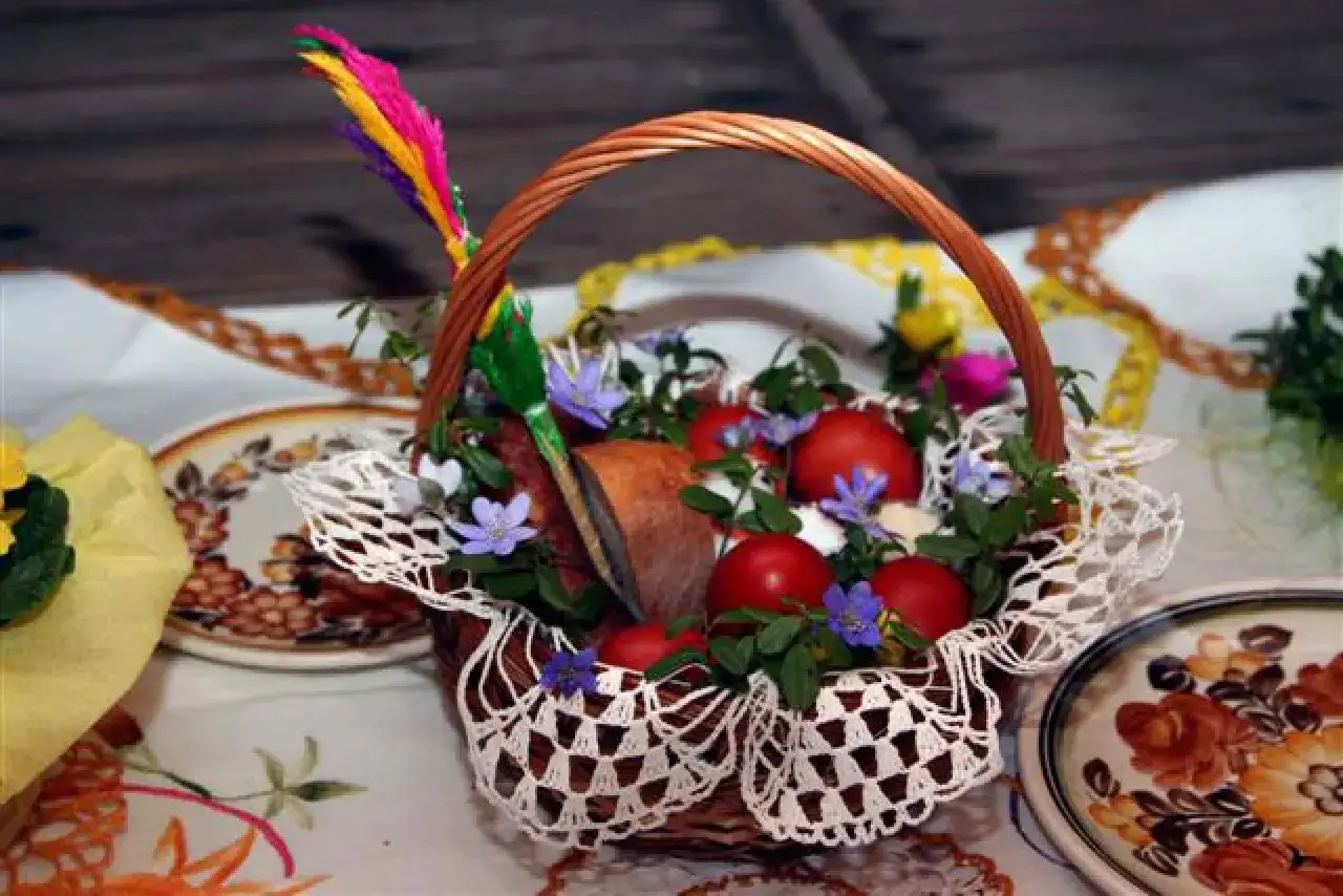 Koszyk z pisankami, kiełbasą i chlebem, ozdobiony kwiatami i pi&oacute;rkiem. Idealny do święconki.