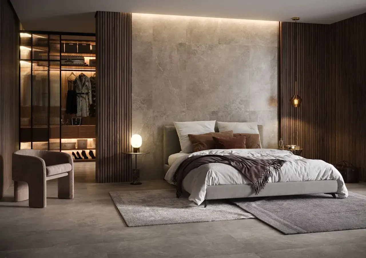 Elegancka sypialnia z widoczną garderobą w sypialni za ścianką. Wnętrze o stonowanej kolorystyce, z łóżkiem i wygodnym fotelem.