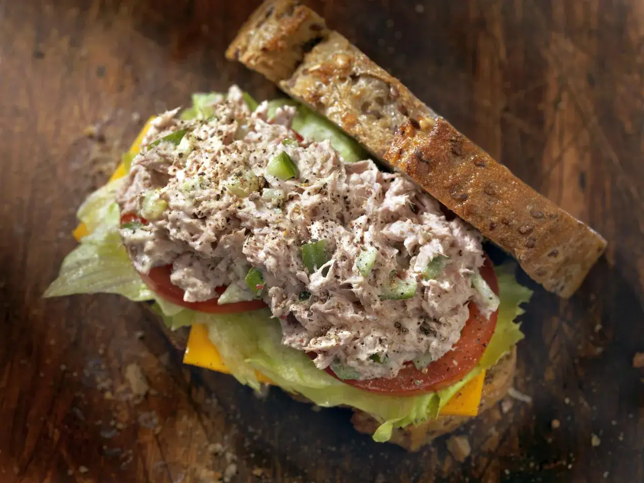 Kanapka z obfitą porcją pasty z tuńczyka, świeżą sałatą, pomidorem i serem na ciemnym pieczywie.