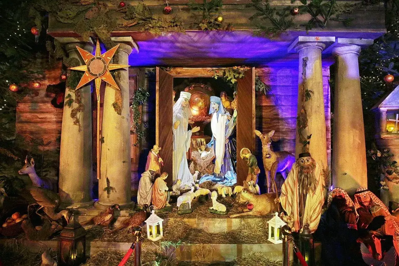 Szopka bożonarodzeniowa z figurkami Świętej Rodziny, pasterzy i zwierząt. W tle gwiazda betlejemska, przypominająca o czasie, kiedy powstała kolęda 