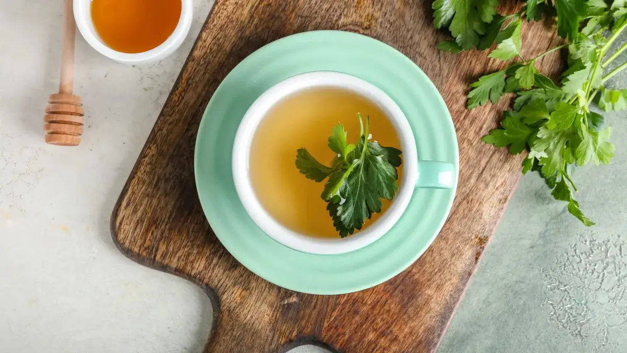 Napar z natki pietruszki, znany ze swoich właściwości, w filiżance z miodem i gałązką ziela.