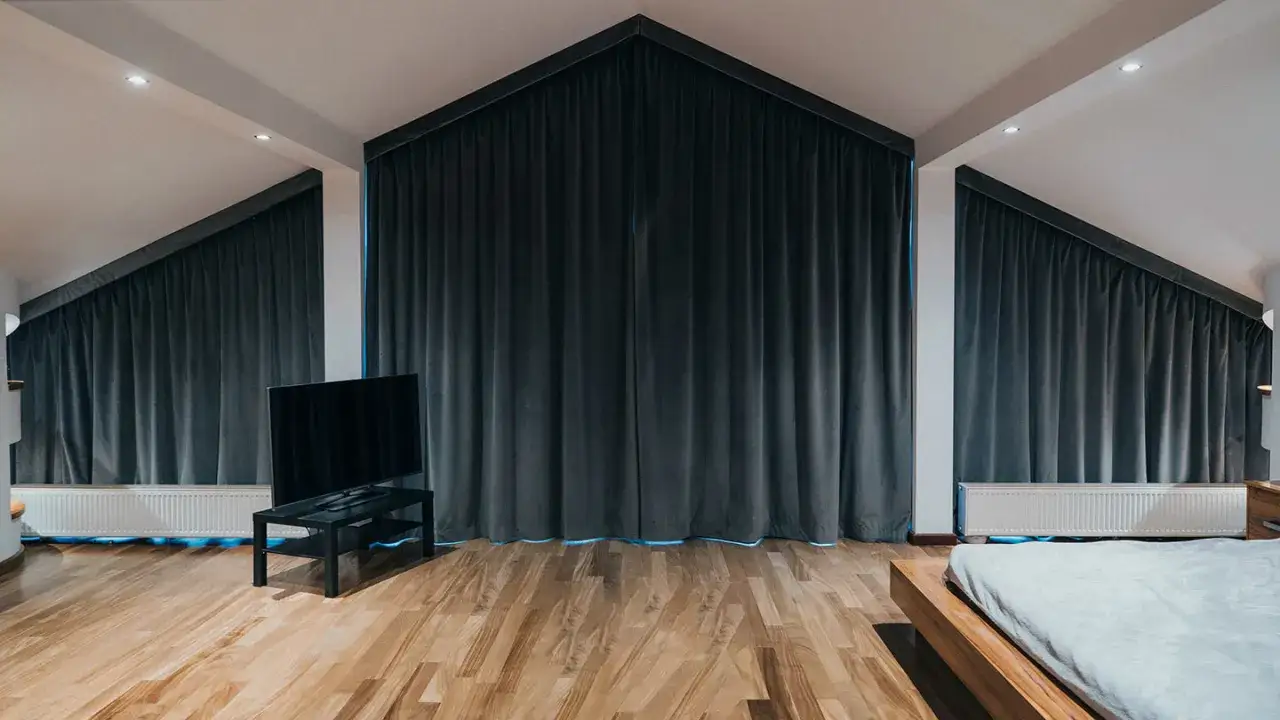 Nowoczesne karnisze na skośne okna idealnie komponują się z ciemnymi zasłonami, tworząc przytulną atmosferę w sypialni.