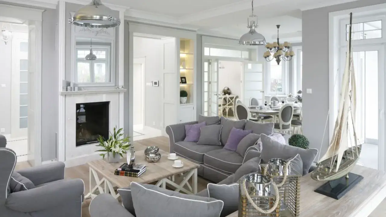 Elegancki kominek w salonie, obok szarej sofy i stolika kawowego z książkami.