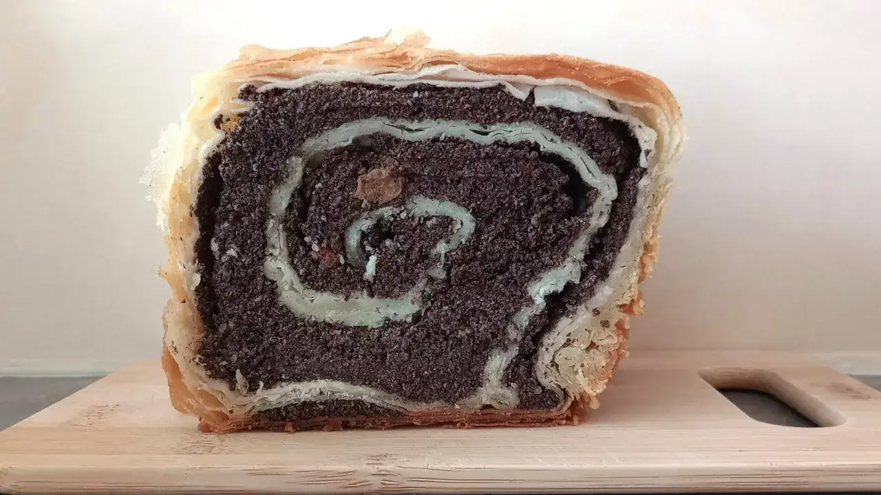 Kawałek ciasta z makiem, z widocznym, spiralnym nadzieniem makowym i jasnozielonymi akcentami, na drewnianej desce.