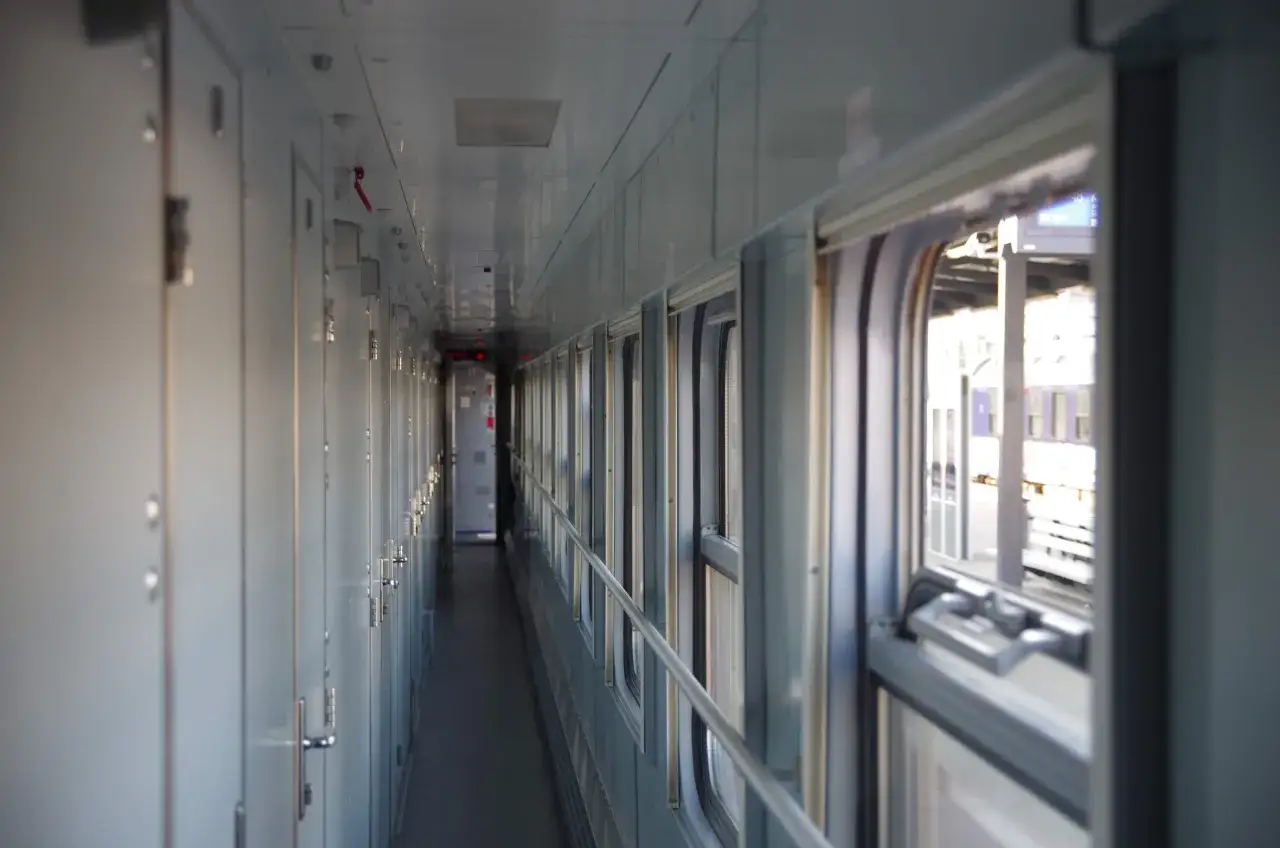 Wnętrze wagonu sypialnego Pendolino. Długi korytarz z drzwiami po lewej i oknami po prawej.