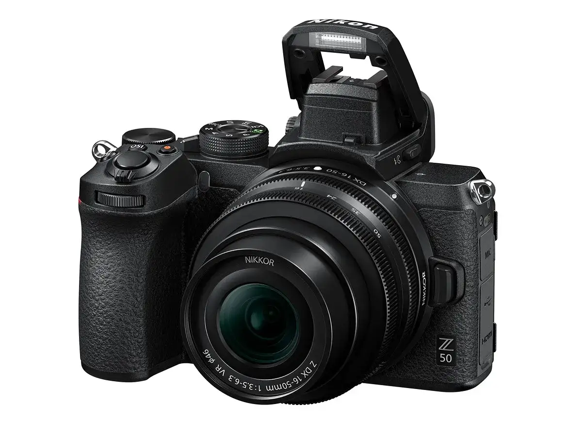 Nikon Z50 test: czarny aparat z obiektywem NIKKOR DX 16-50mm, wysuniętą lampą błyskową i uchwytem.
