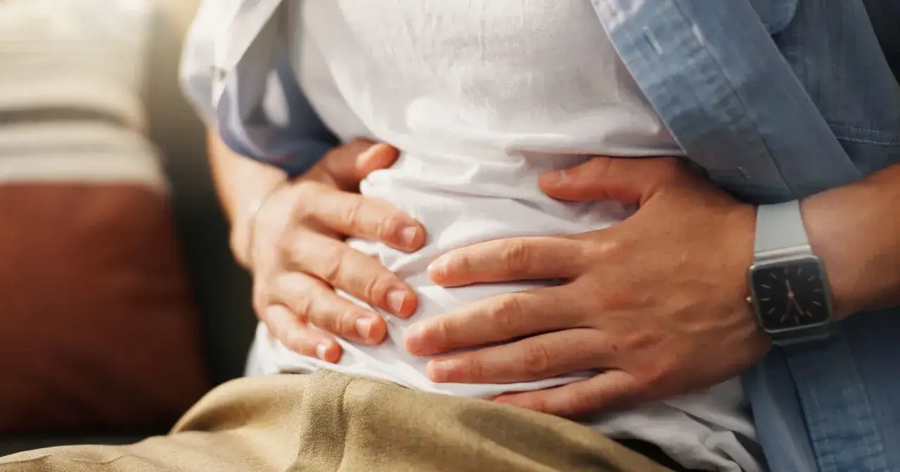 Osoba trzyma się za brzuch, odczuwając nieprzyjemne uczucie pełności w brzuchu.