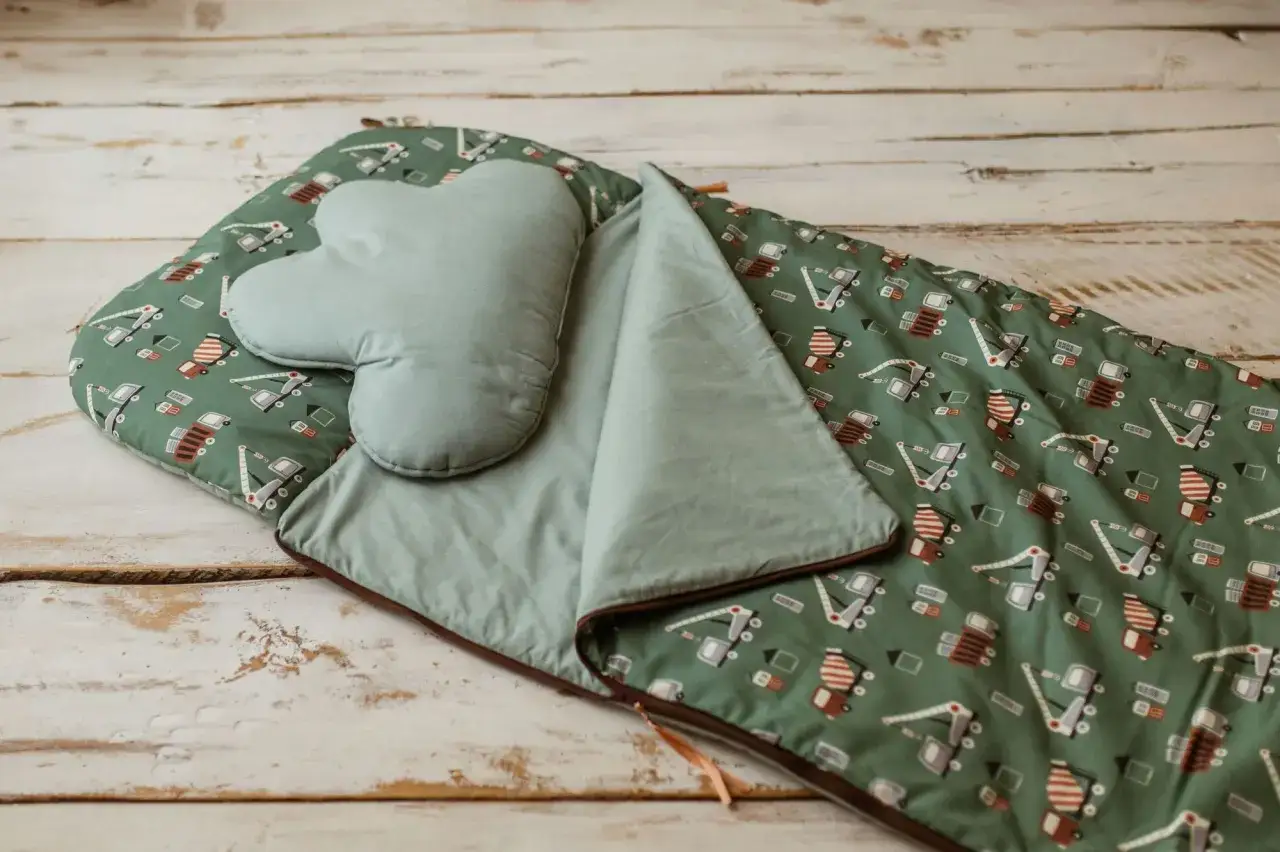 Zielony śpiwór do przedszkola z motywem budowlanym i serduszkową poduszką. Idealny na drzemki.