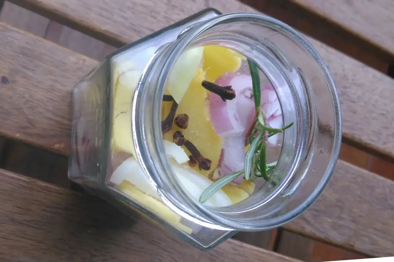 Słoik z plastrami cebuli, goździkami i rozmarynem. Powstaje naturalny syrop z cebuli na przeziębienie.
