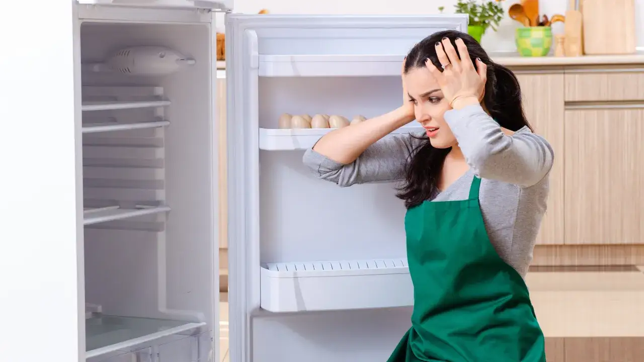 Kobieta z rozpaczą chwyta się za głowę, patrząc na puste półki lodówki. Czyżby uszkodzony agregat w lodówce objawy były tak poważne?