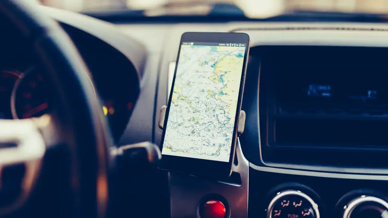 Telefon z mapą na ekranie zamontowany w samochodzie. Kierowca korzysta z telefonu podczas jazdy, co jest niebezpieczne.