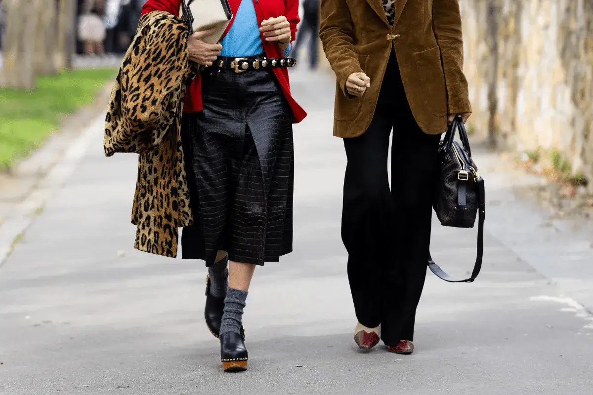 Dwie kobiety w stylu moda lata 70. Jedna w panterce, czerwonej marynarce i czarnej sp&oacute;dnicy, druga w brązowej marynarce i szerokich spodniach.