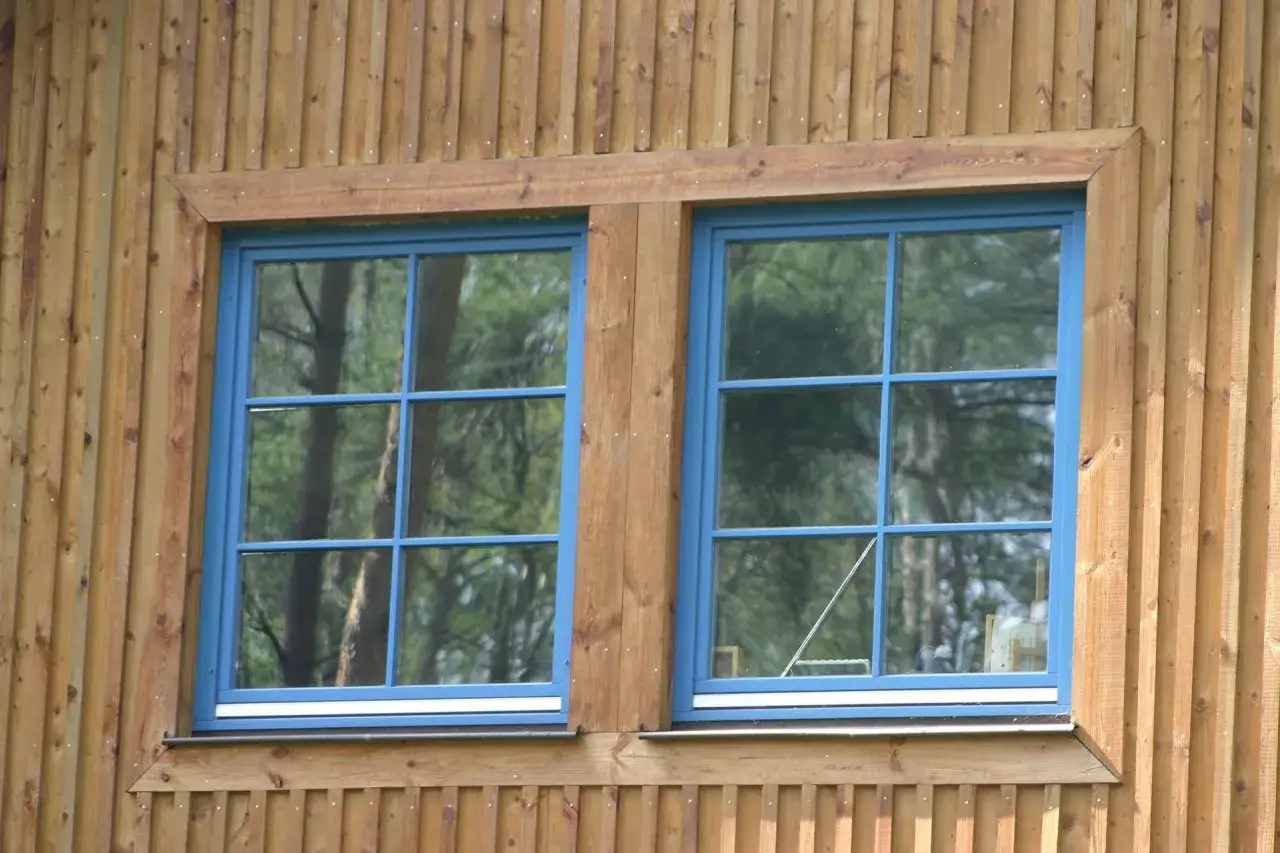 Dwa niebieskie okna drewniane ze szprosami w drewnianej elewacji.