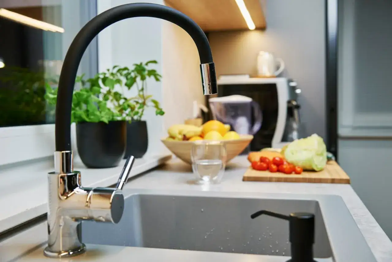 Czarny dozownik na płyn do naczyń w zlewie, obok kranu i świeżych warzyw.