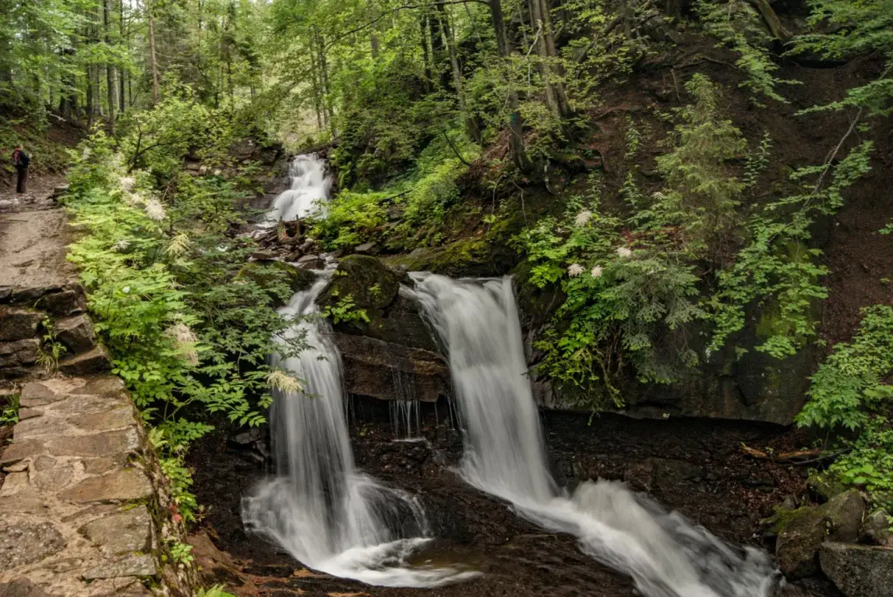 Szlak prowadzi przez las do wodospad&oacute;w. W oddali widać turystę, kt&oacute;ry zastanawia się, skąd na Baranią G&oacute;rę.