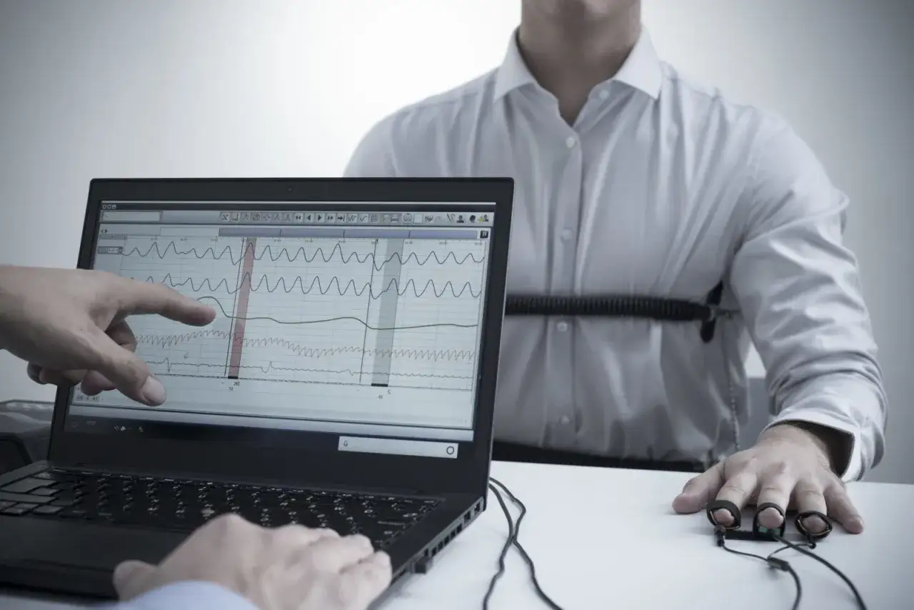 Badanie wykrywaczem kłamstw w Warszawie. Na ekranie laptopa wykresy fizjologiczne, a na mężczyźnie pas do poligrafu.