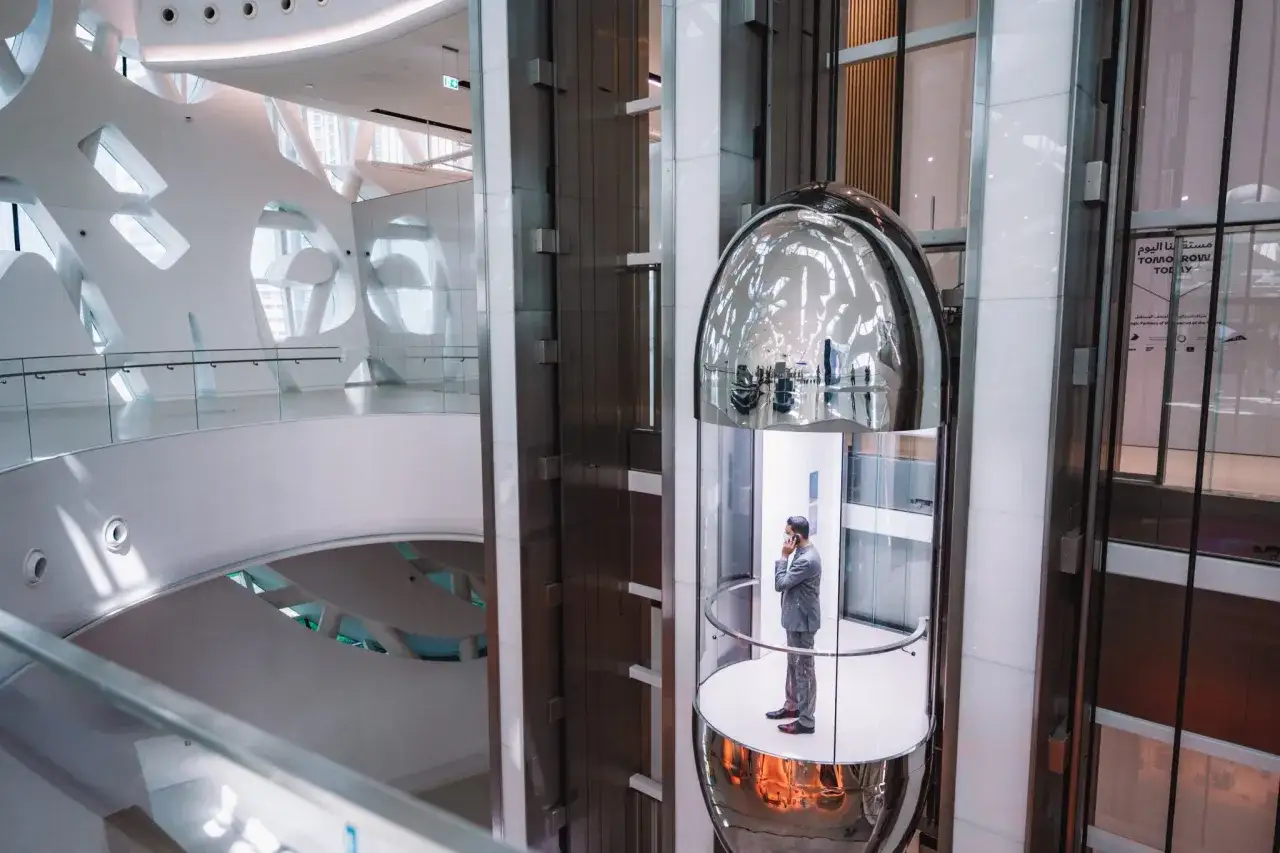 Mężczyzna w garniturze rozmawia przez telefon w szklanej windzie w futurystycznym wnętrzu Dubaj Muzeum Przyszłości.