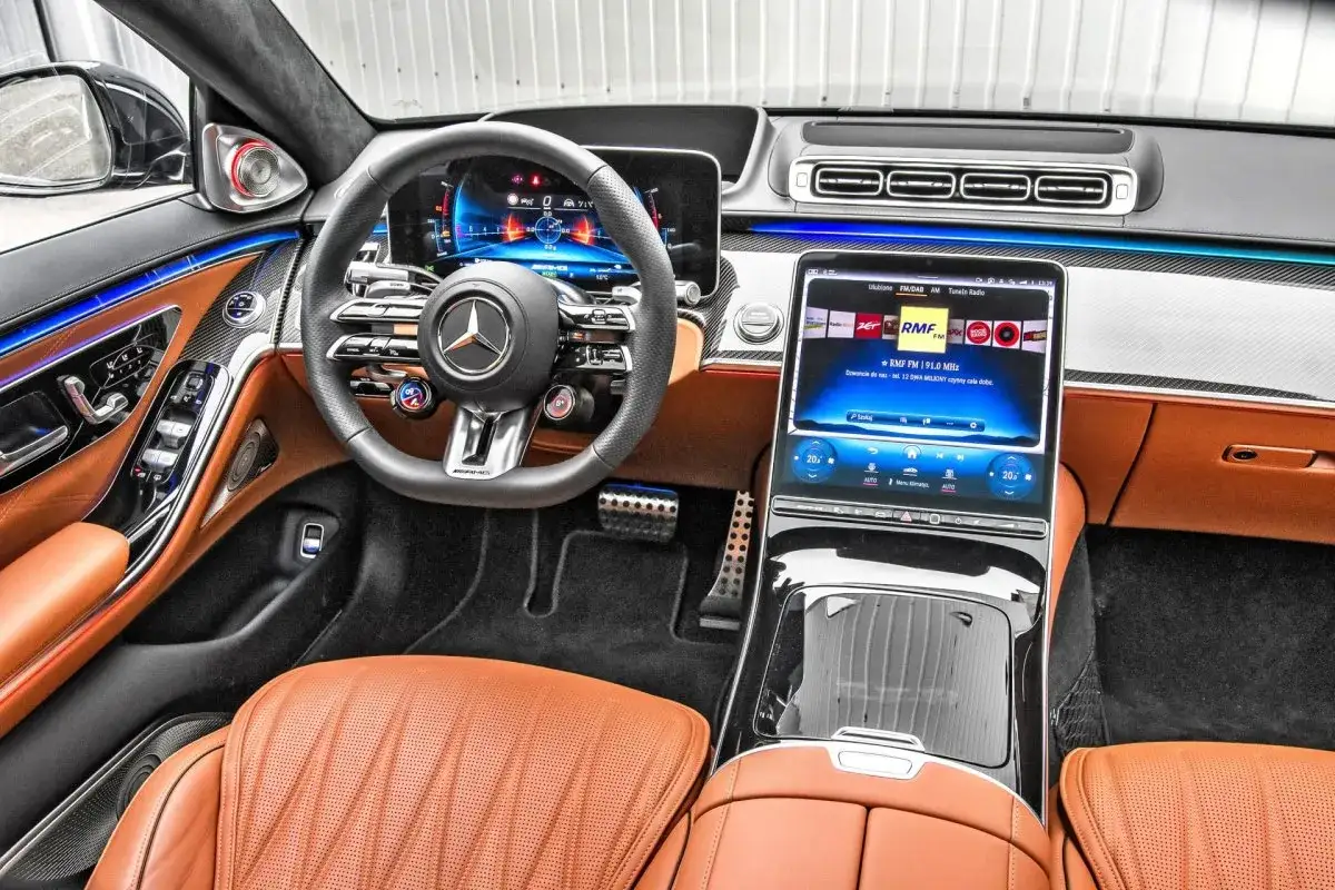 Wnętrze S 63 AMG Mercedes-Benz z brązową skórzaną tapicerką, nowoczesnym ekranem i ambientowym oświetleniem.