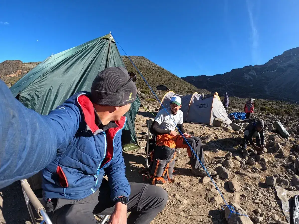 Grupa turystów rozbija obóz na drodze na Kilimandżaro. W tle góry i namioty.