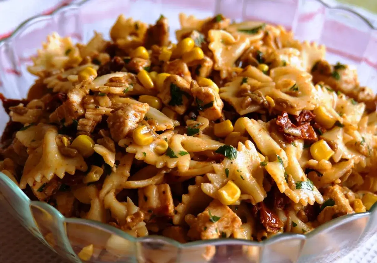 Pyszna sałatka makaron z kurczakiem, kukurydzą i suszonymi pomidorami w szklanej misie.