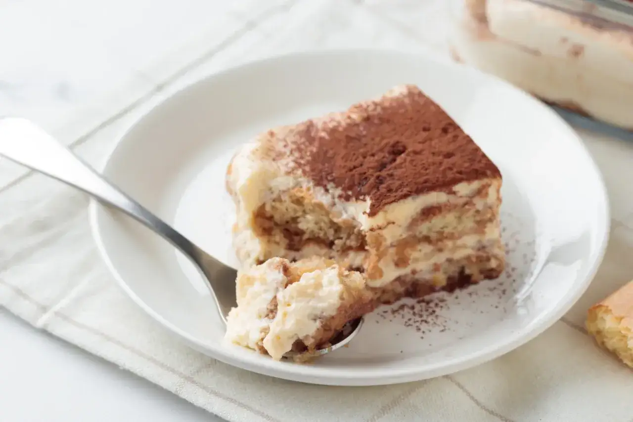 Pyszne tiramisu Ani gotuje, z kakaową posypką i kremowym nadzieniem, czeka na widelcu.