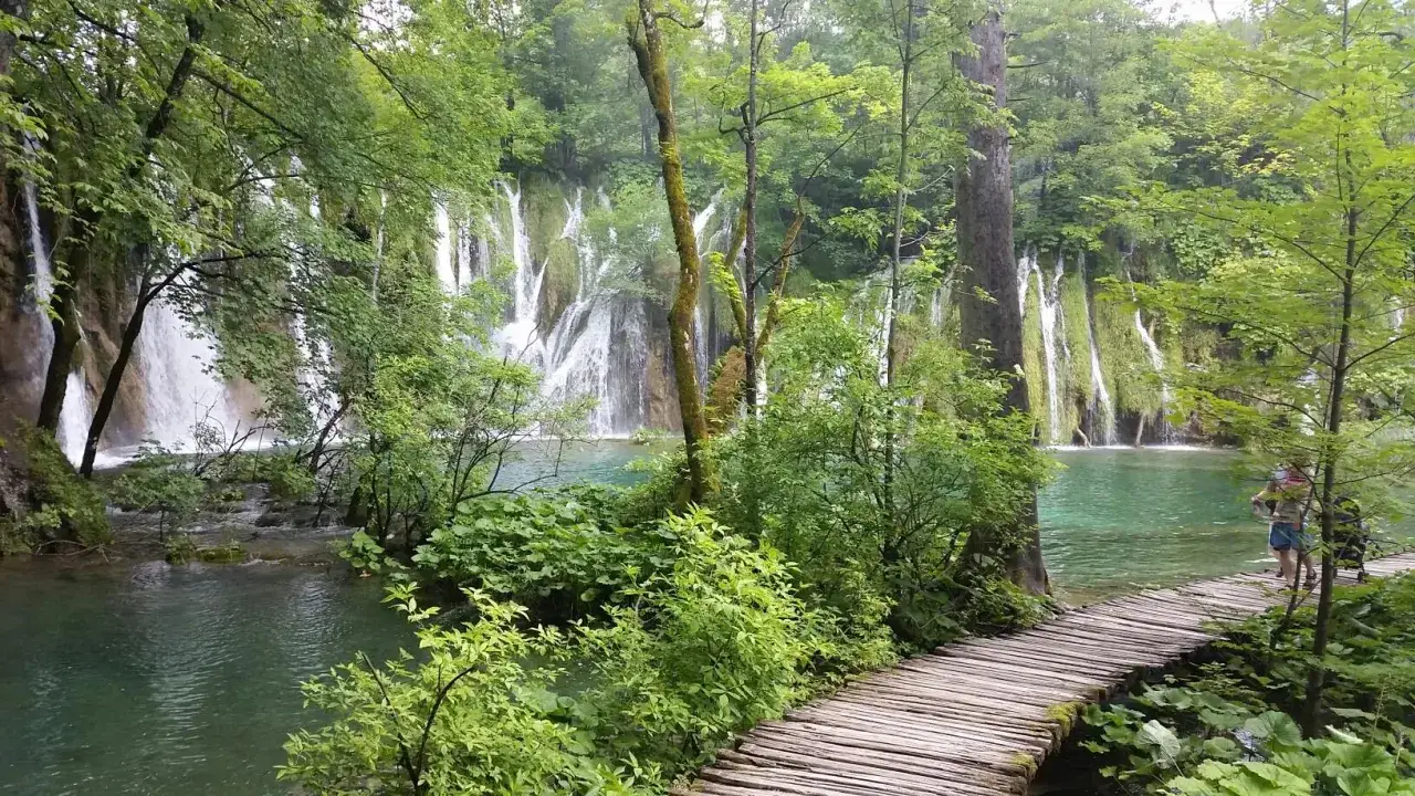Malownicze wodospady w Alpach Dynarskich, turkusowa woda i drewniana kładka wśród bujnej zieleni.