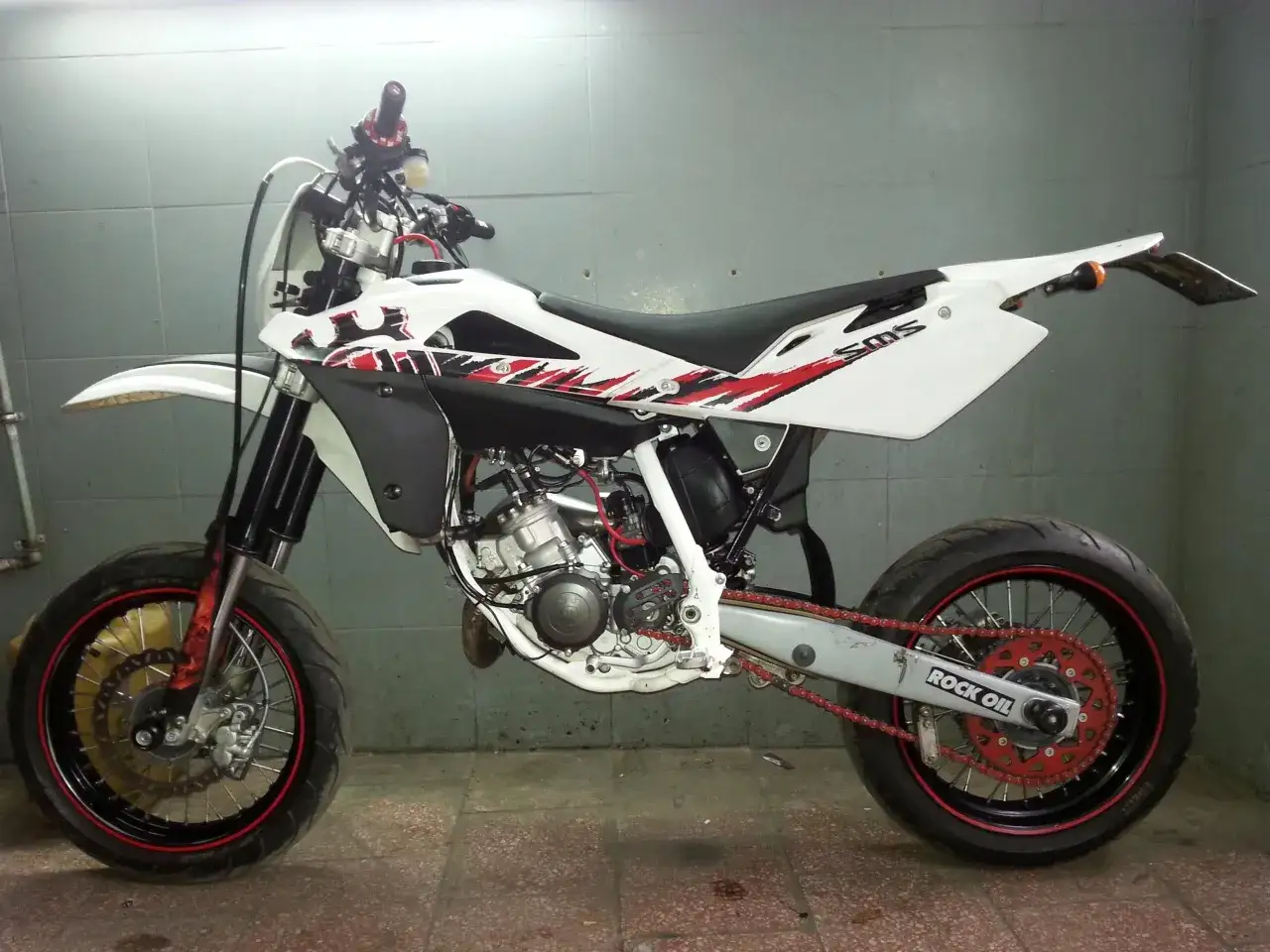 Biały motocykl Husqvarna 125 supermoto z czerwonymi akcentami i napędem. Gotowy do jazdy po torze.