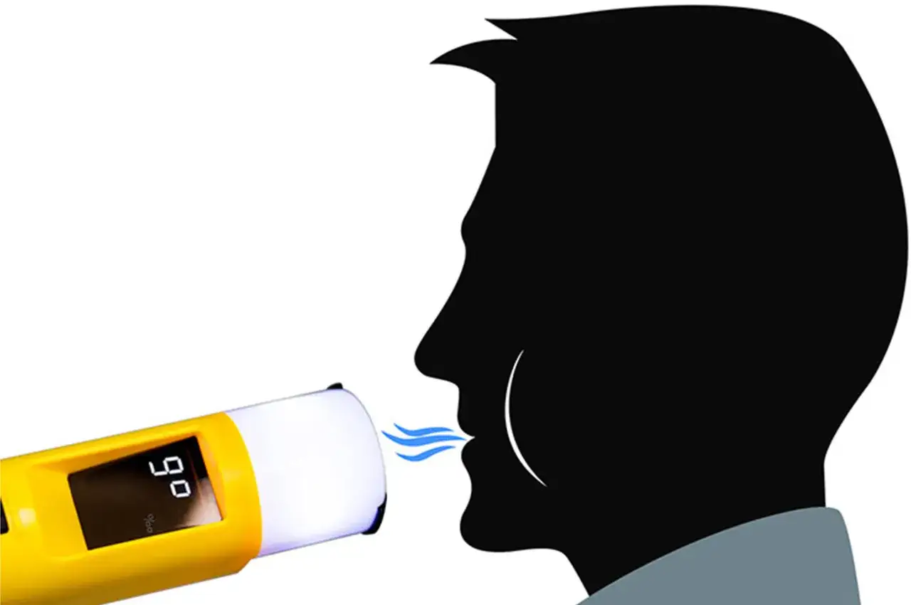 Alkomat pokazuje 0,90 mg/l. Mężczyzna dmucha w urządzenie, sprawdzając zawartość alkoholu w wydychanym powietrzu.