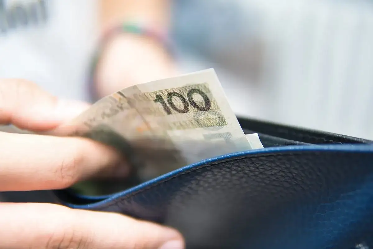 Dłoń wkłada banknot 100 zł do portfela. To symbol wolności finansowej i konto bez komornika.