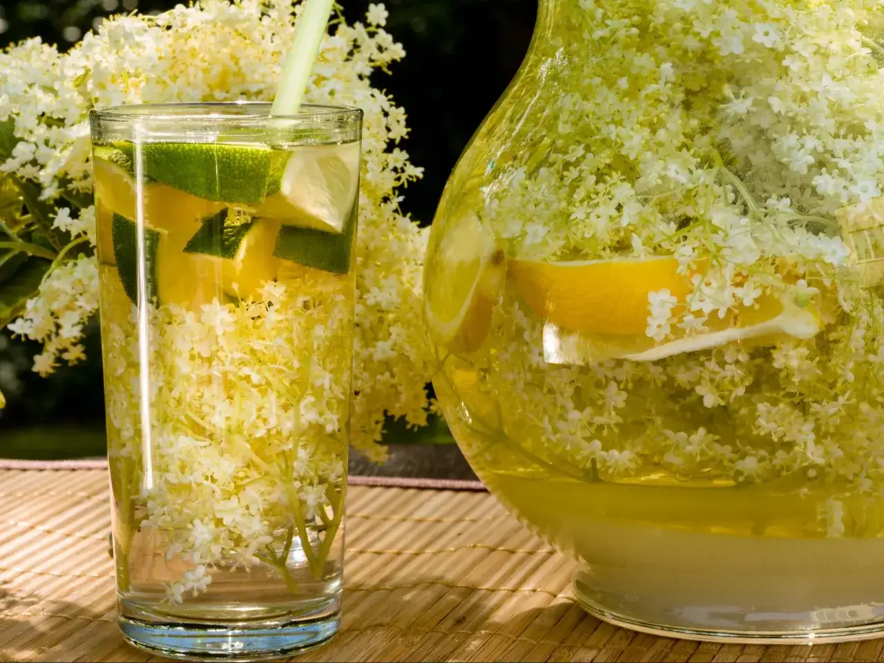 Orzeźwiająca lemoniada z kwiatów czarnego bzu, z plasterkami cytryny i limonki, podana w szklance i dzbanku.
