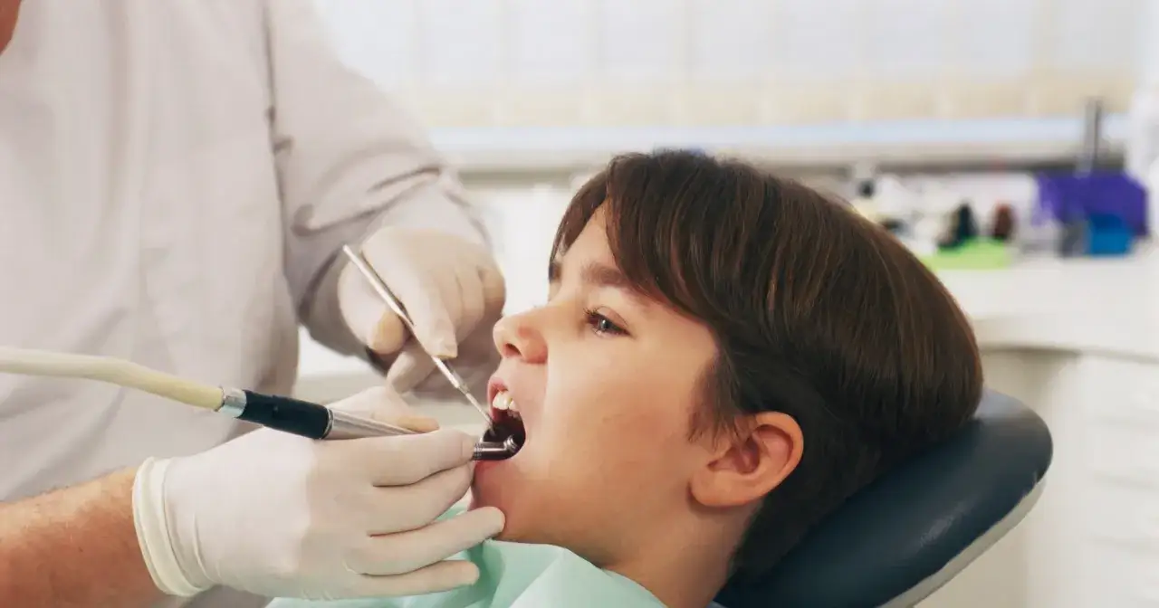 Chłopiec przechodzi zabieg lakierowania zęb&oacute;w u dzieci. Dentysta w rękawiczkach używa narzędzi stomatologicznych.