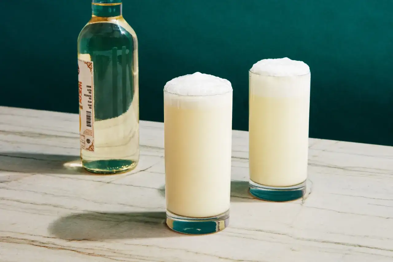 Dwa puszyste drinki gin fizz z butelką ginu w tle, gotowe do orzeźwiającej chwili.