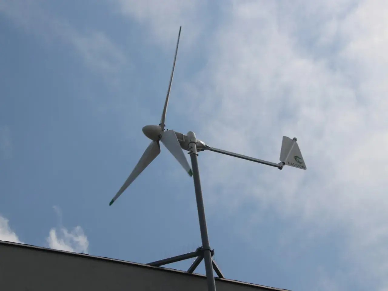 Mały wiatrak OZE na dachu, z zielonymi końc&oacute;wkami łopat i logo 