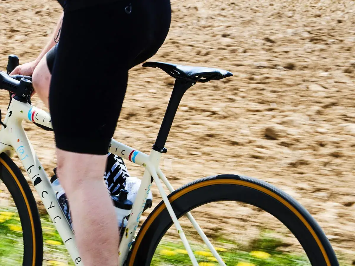 Kolarz w czarnych spodenkach na białym rowerze. Właściwe dopasowanie roweru to klucz do komfortowej jazdy.