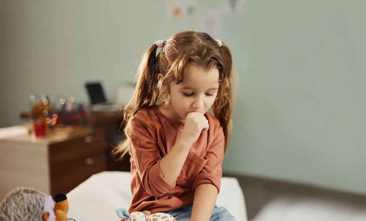 Mała dziewczynka z dwoma kucykami, kaszląca do ręki, może mieć krztusiec u dzieci.