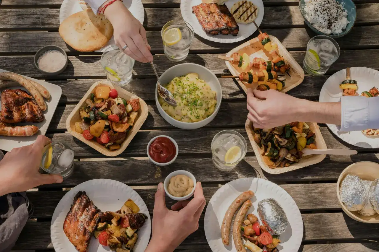 Pyszne jedzenie na grilla: żeberka, kiełbaski, szaszłyki z warzywami i ziemniaki w folii. Słońce, st&oacute;ł i apetyczne dania.
