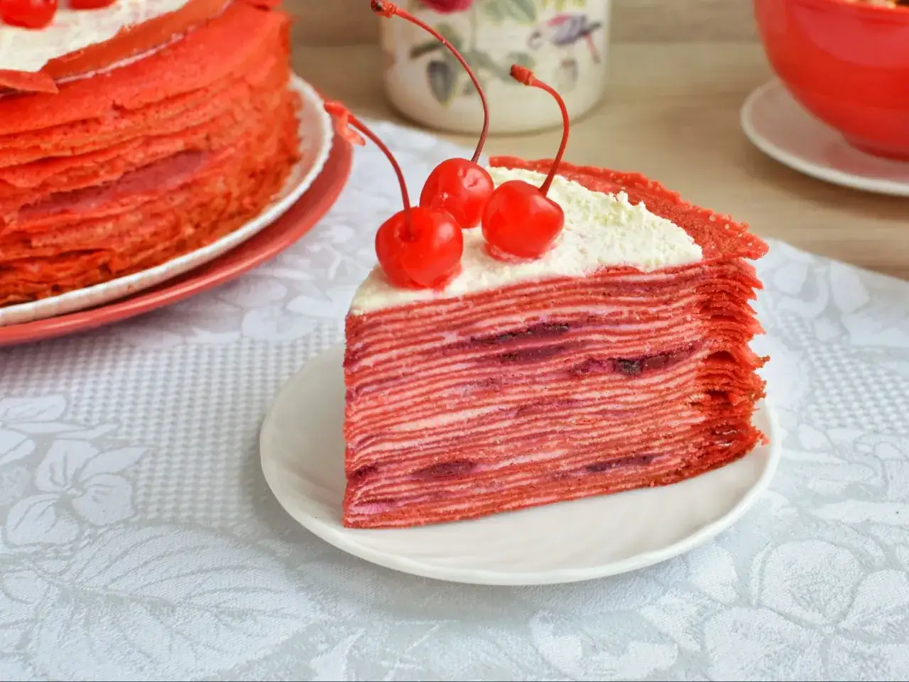 Kawałek tortu red velvet z kremem i wiśniami, ułożony na talerzyku.
