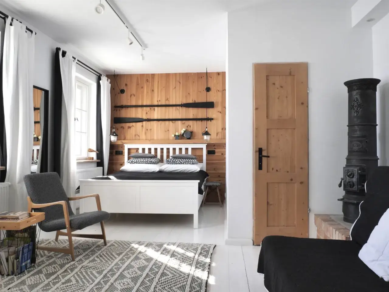 Przytulne trzy morza apartamenty pod Tr&oacute;jmorskim Wierchem. Drewniana ściana, białe ł&oacute;żko, wygodny fotel i piec koza.