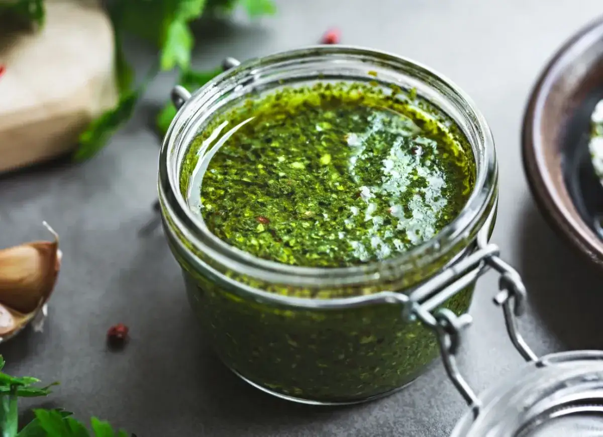 Słoik pełen aromatycznego sosu bazyliowego do makaronu, obok czosnek i świeże zioła.