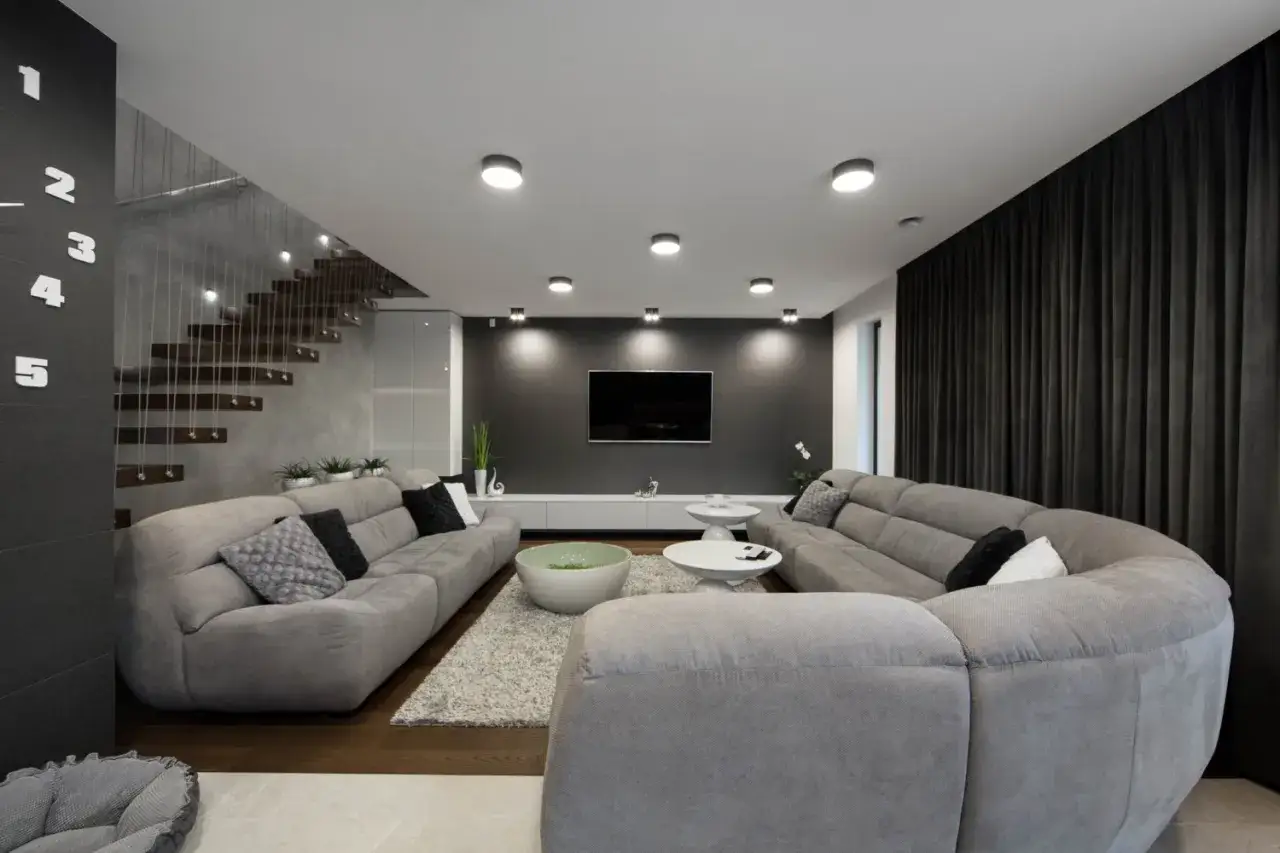 Nowoczesne urządzenie pokoju z szarymi sofami, dywanem, schodami i telewizorem.