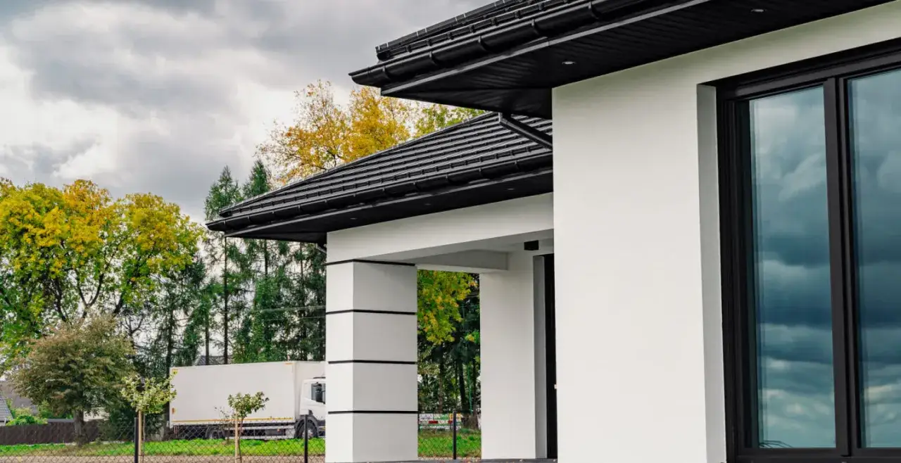 Nowoczesny dom z białymi ścianami i grafitowym dachem. Elegancka podbitka idealnie komponuje się z całością, tworząc sp&oacute;jną, stylową bryłę.