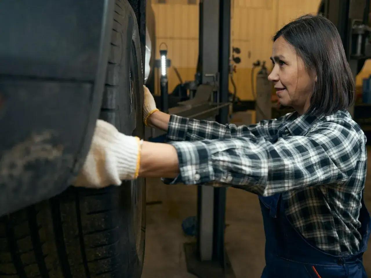Mechaniczka w białych rękawiczkach sprawdza oponę, nasłuchując ewentualnego stukania w kole.