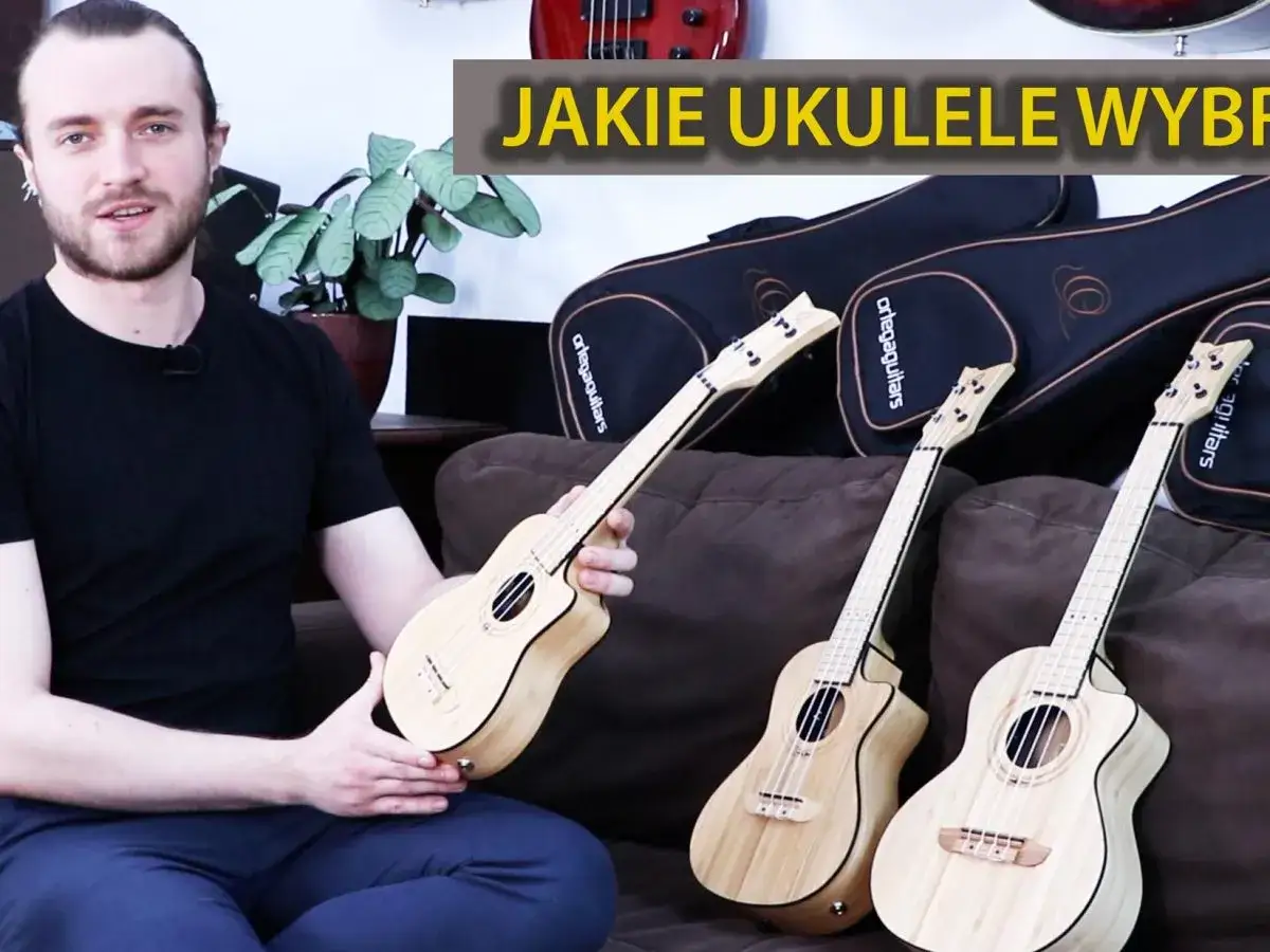 Mężczyzna prezentuje, co to jest ukulele. Na kanapie leżą trzy drewniane ukulele, a za nimi widoczne są czarne pokrowce.