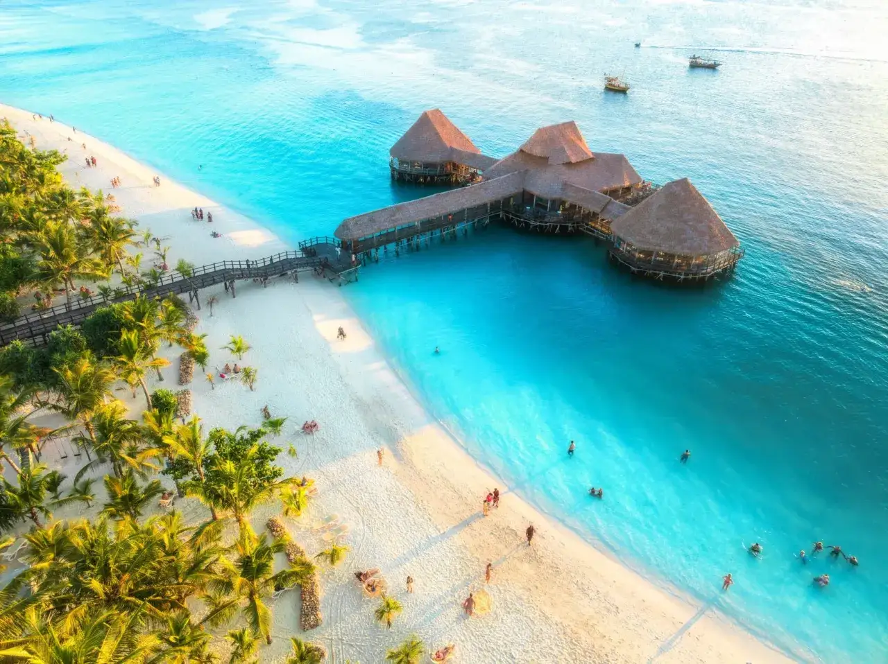 Rajska plaża z palmami i turkusową wodą. W oddali restauracja na palach, idealne miejsce na Zanzibar na własną rękę.