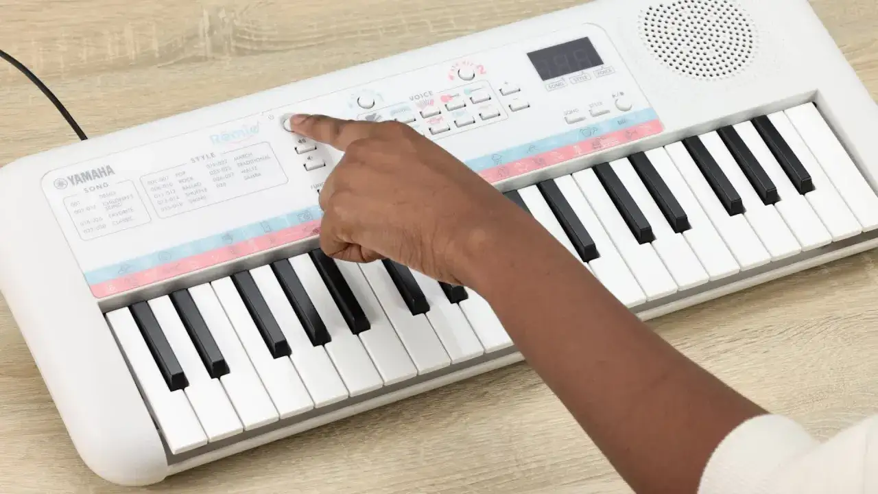 Dziecko uczy się grać na białym keyboardzie Yamaha Remie, wybierając utwory i style.