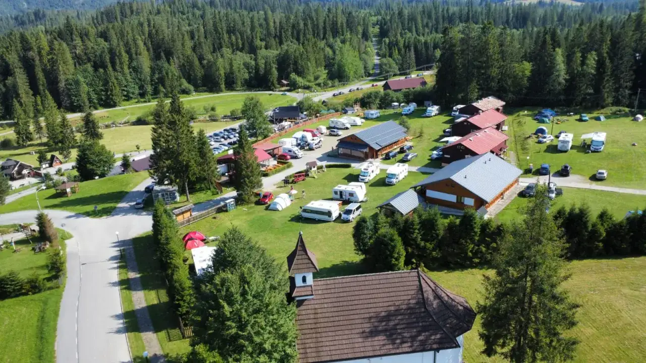 Malowniczy camping Oravice otoczony lasem, pełen przyczep kempingowych i kamper&oacute;w. Widać budynki, namioty i parking.