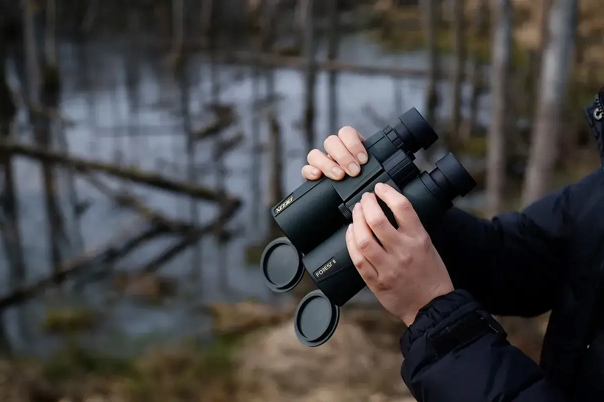 Ręce trzymają lornetkę Delta Forest II, idealną do obserwacji przyrody. Doskonała lornetka w g&oacute;ry.
