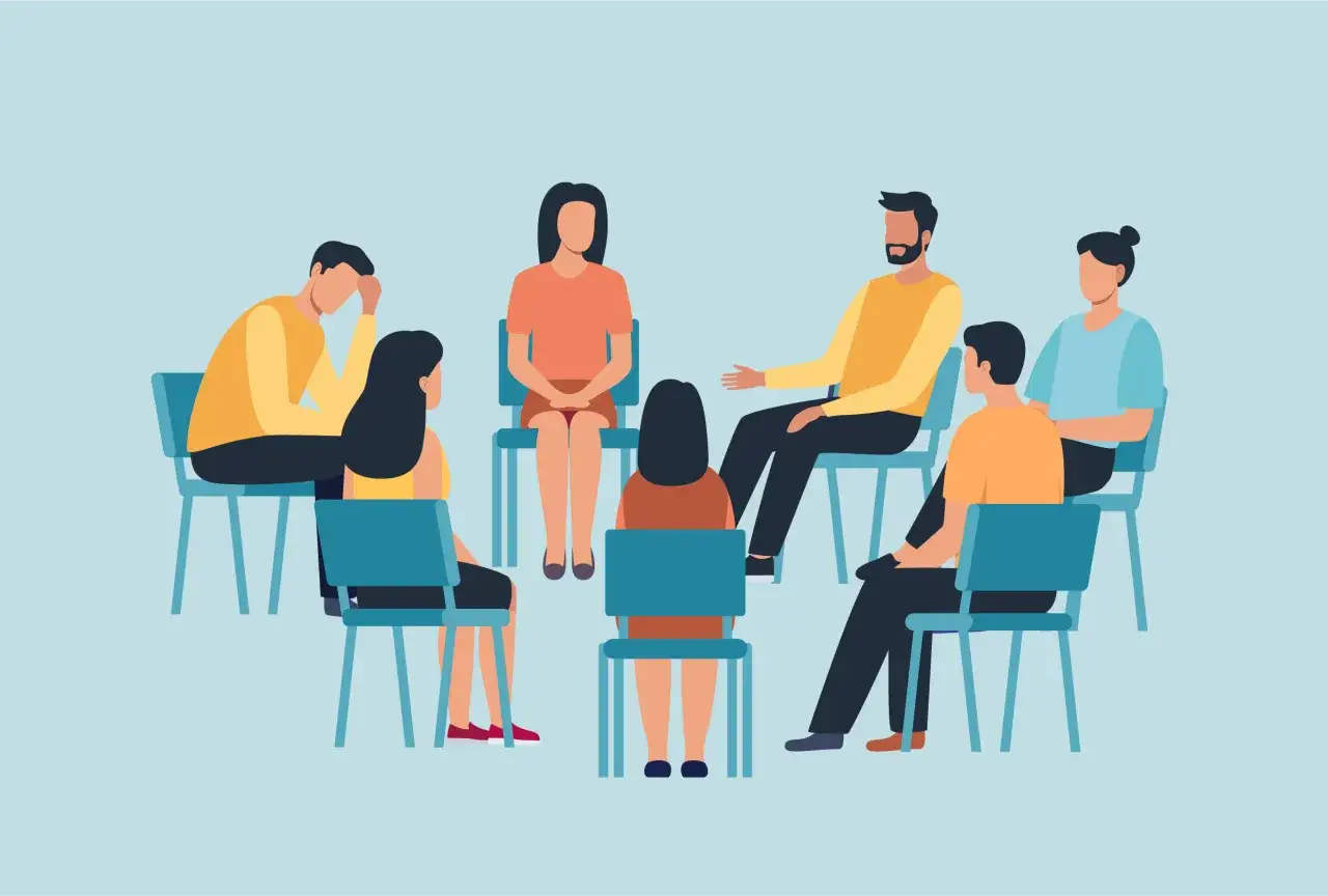 Grupa ludzi siedzi w kręgu, wspierając się nawzajem. Pokazuje, jak postępować z osobą chorą psychicznie, oferując zrozumienie i pomoc.