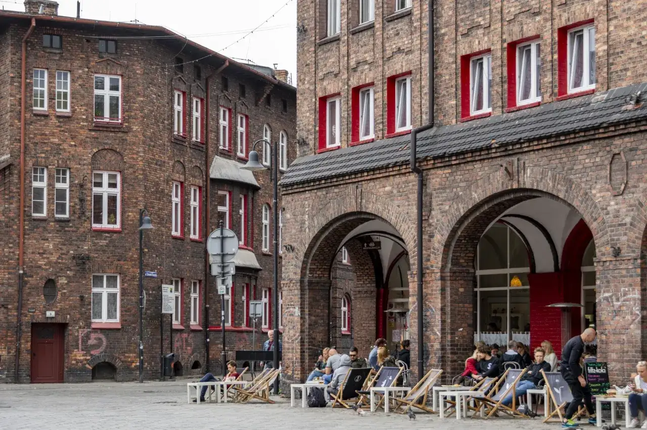 Ludzie odpoczywają przy kawiarni w ceglanych budynkach. Idealne miejsce, by sprawdzić, gdzie rezerwować noclegi w okolicy.
