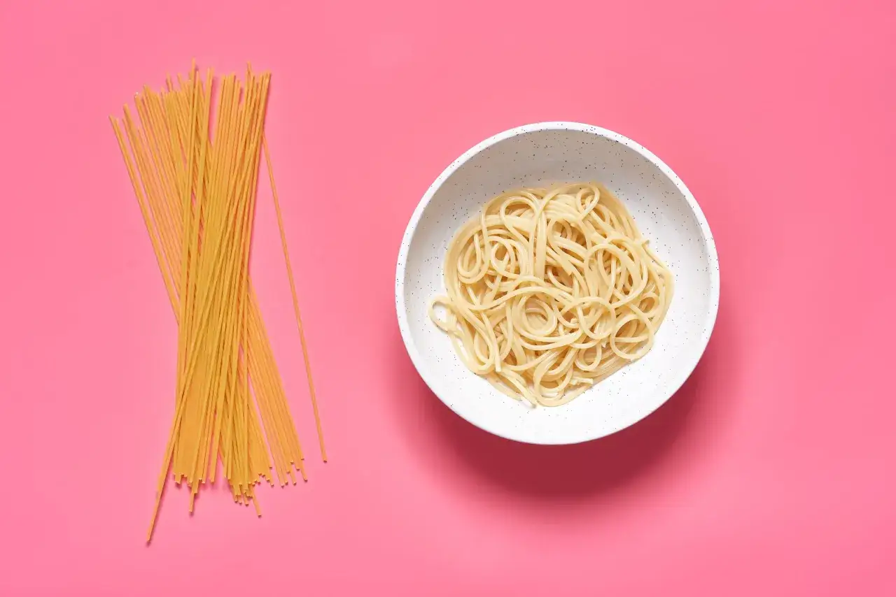 Surowe i ugotowane makarony spaghetti na różowym tle. Zastanawiasz się, jaki makaron spaghetti kcal po ugotowaniu będzie miał Twój posiłek?